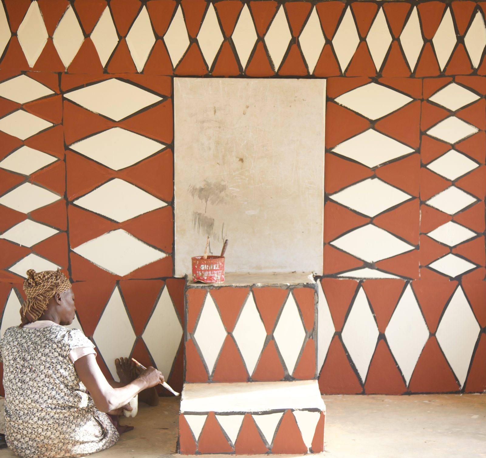 A member of SWOPA, seated on the floor, paints a wall of red and white diamond patterns