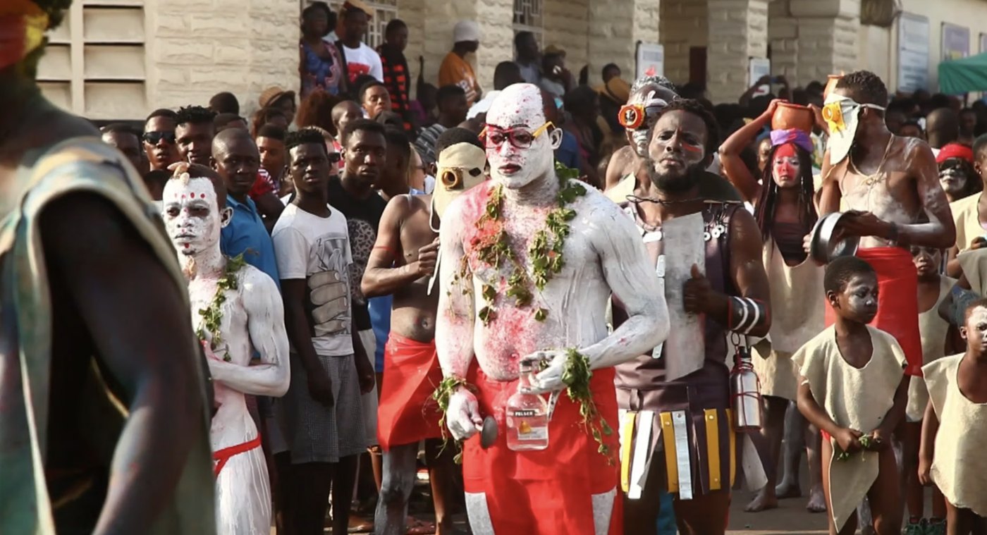 A still from Agbako, 2015: painted performers in a street procession
